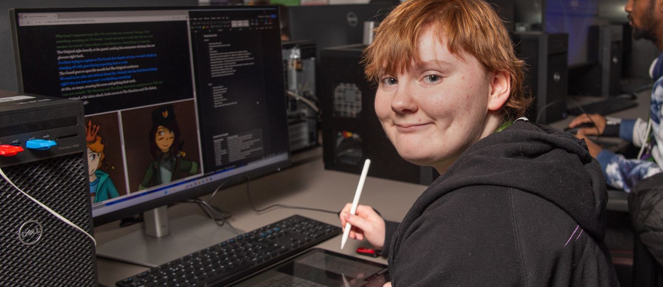 Graphic Design student at SBC drawing in their book in front of a computer
