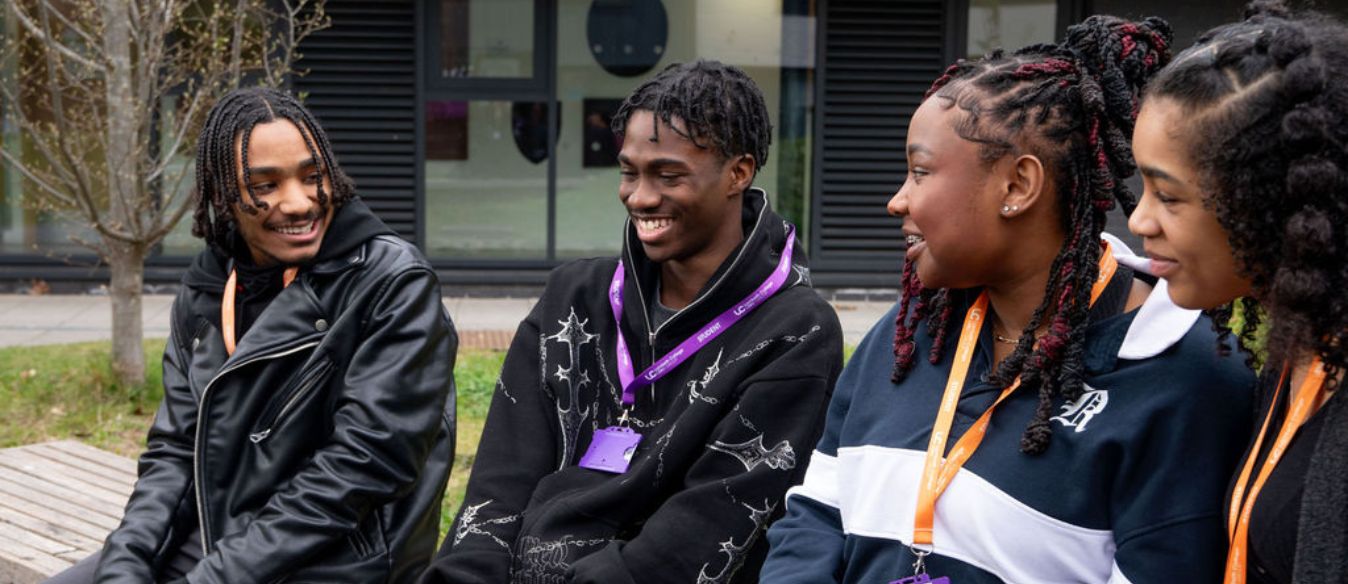 Four young people sit on a bench, smiling and enjoying each other's company in a cheerful outdoor setting.