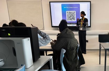 A woman stands before a classroom, delivering a presentation while students attentively listen and take notes